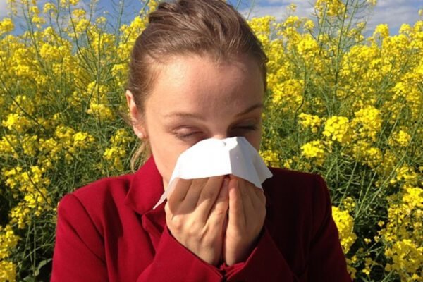 a woman blowing her nose in front of yellow flowers