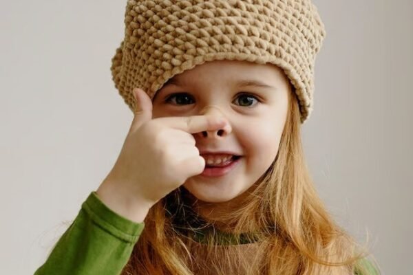 a girl wearing a hat pointing to her nose