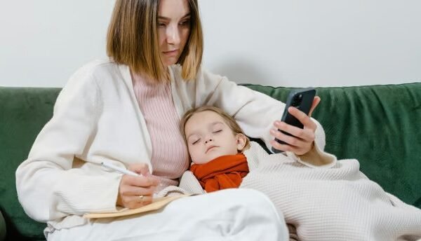 a woman holding a phone and sleeping sick child